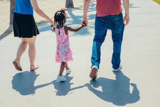 A diverse family enjoying a sunny day, holding hands and walking together.